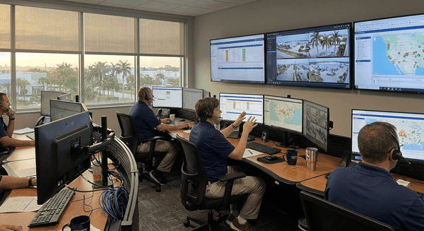 Professional monitoring center with operators at workstations with multiple screens showing alarm dashboards